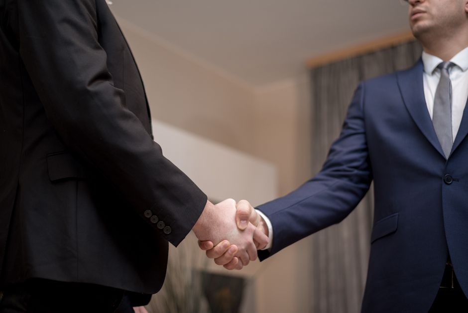 Dva poslovna čovjeka u odijelima rukuju se u uredu, naglašavajući povjerenje i partnerstvo
