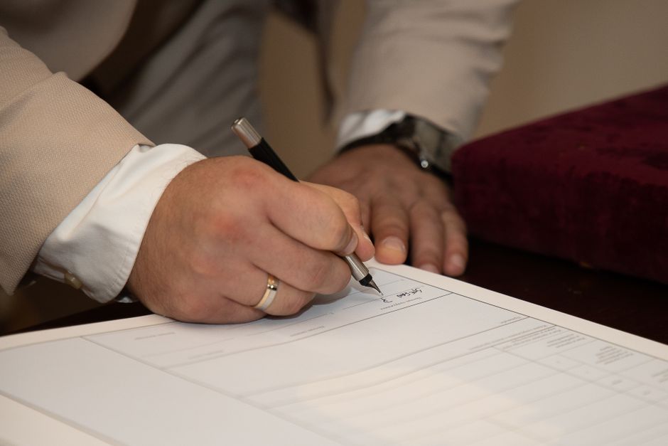 Close-up of a man signing dokument s vjenčanim prstenom i kemijskom olovkom.